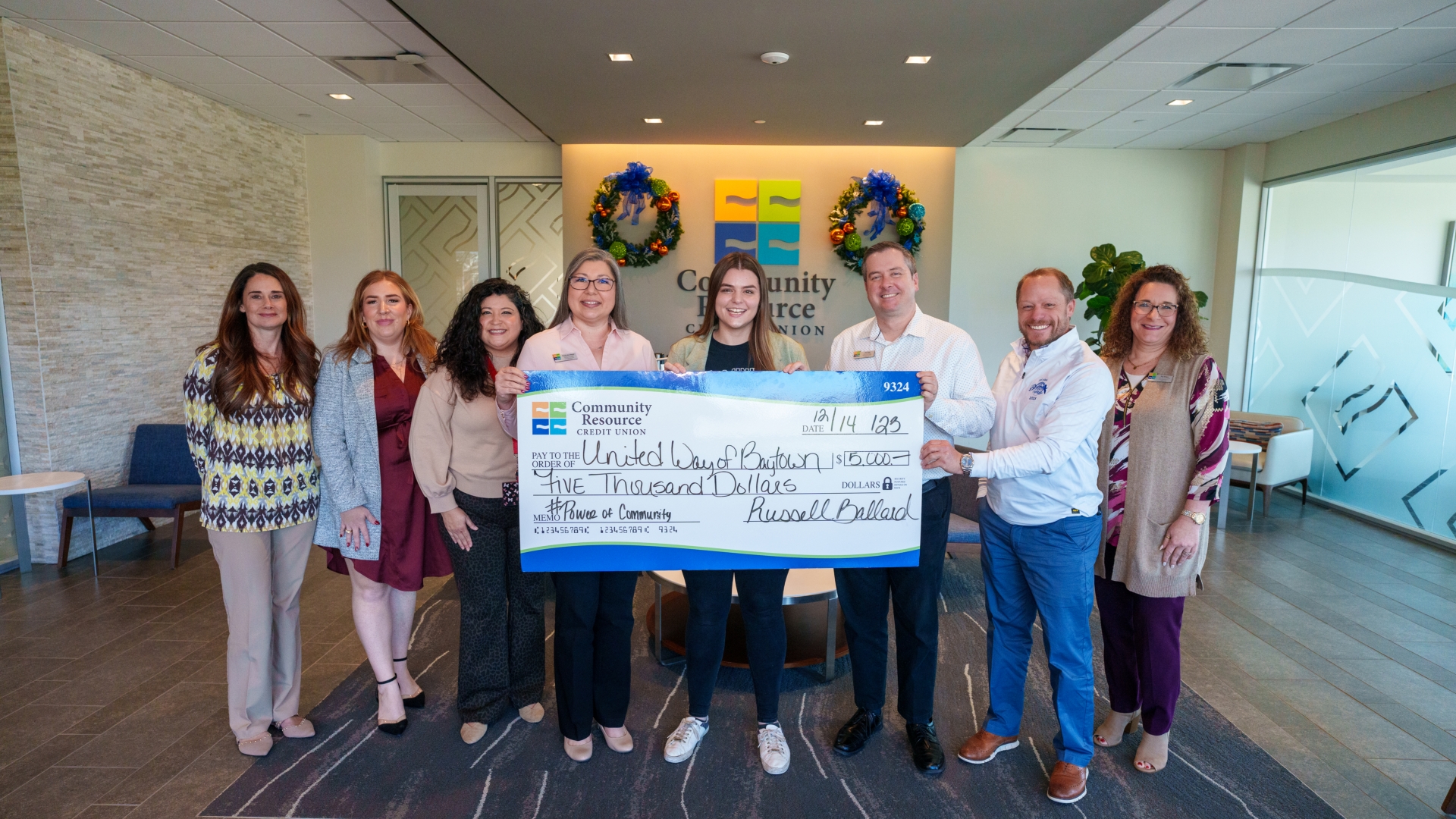 A group of CRCU employees standing together and holding a check.
